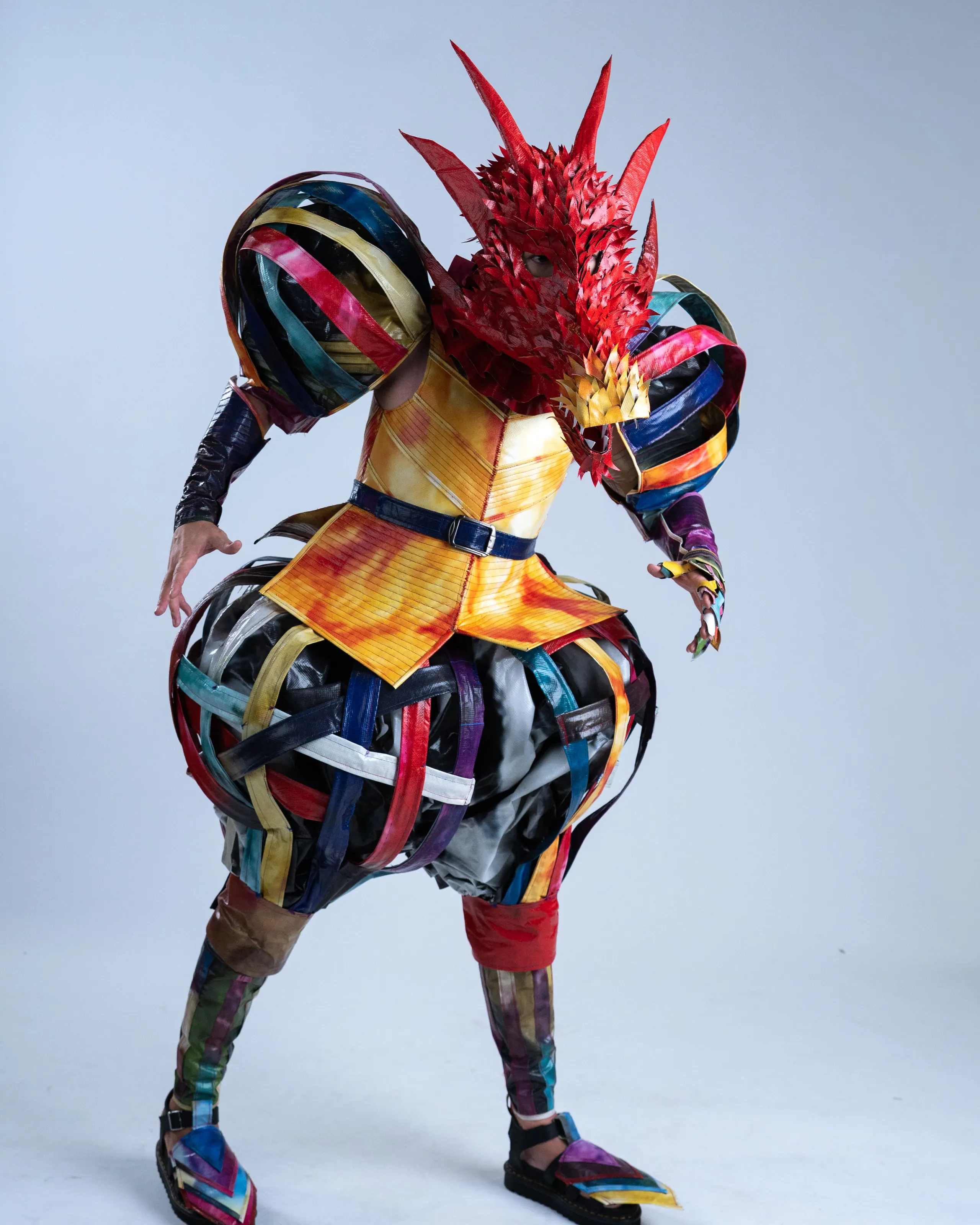 The HOM Art Pop dragon look: a spiked red dragon head and a striped rainbow suit with huge puffed sleeves and trousers, crouched with claws out