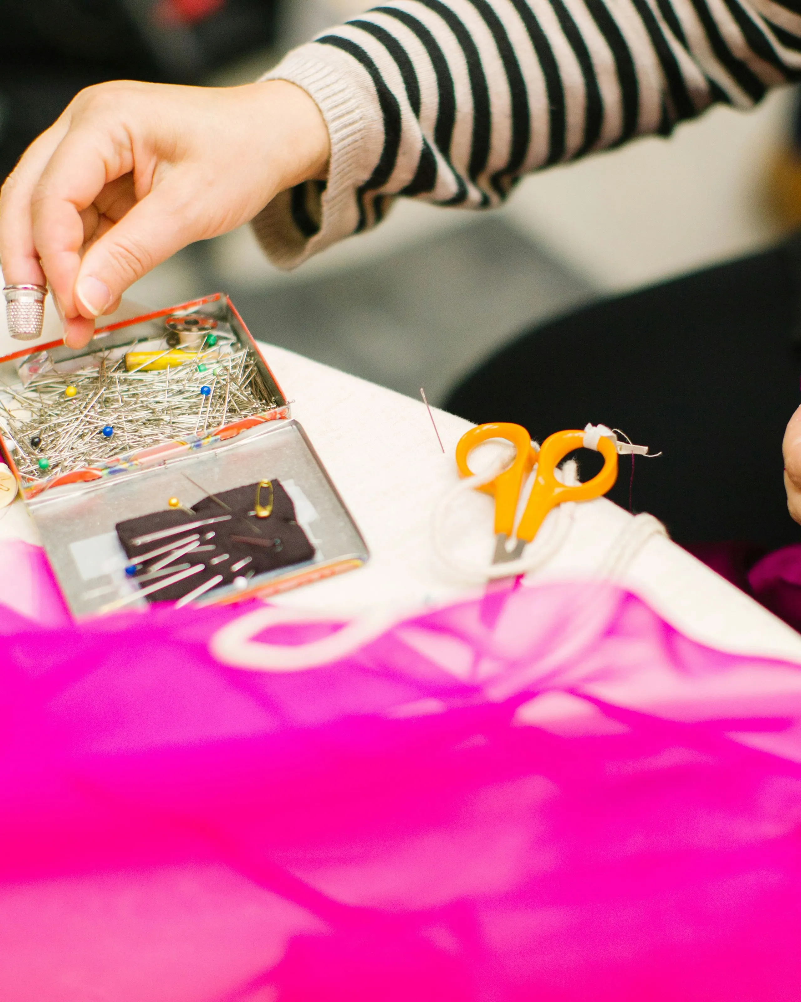Hands pinning bright pink mesh fabric at a work table