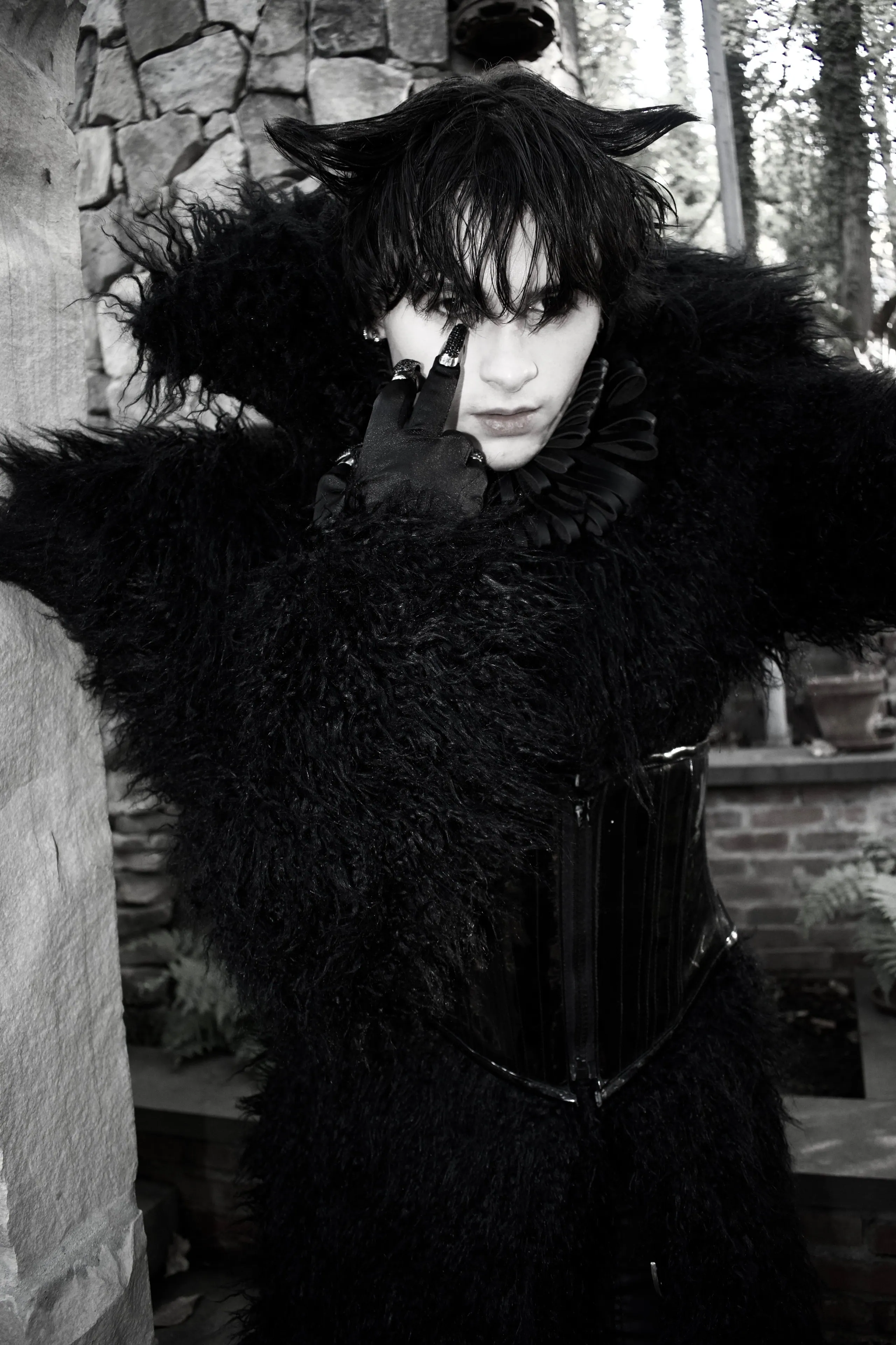 Black and white portrait in a black shag fur coat with a ruff collar, one gloved finger at the eye