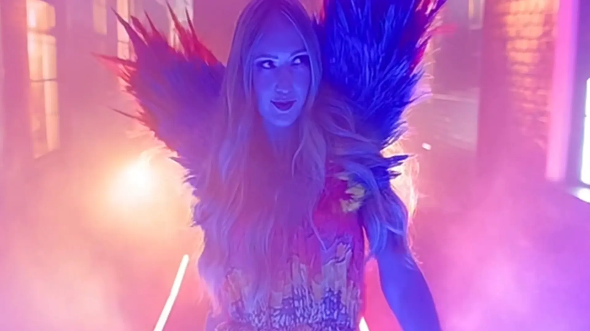 Model in a feathered winged look walking toward the camera through pink smoke