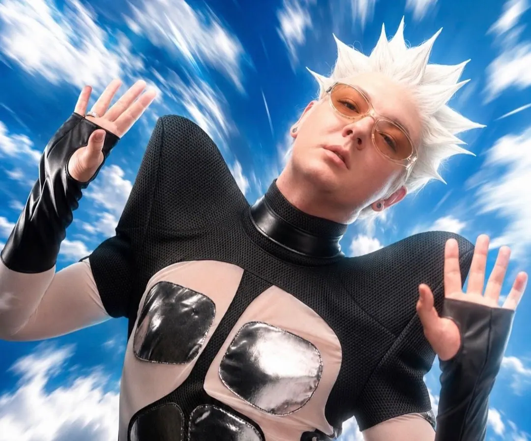 The winged top with chrome chest panels, hands raised against a streaked sky